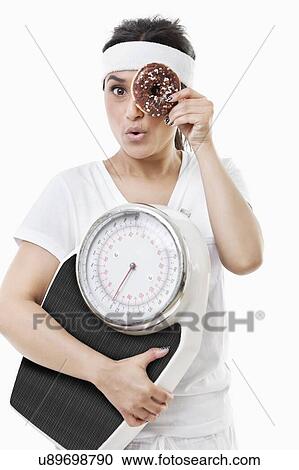 Portrait of young woman looking through donut holding weight scale over white background View Large Photo Image Stock Image - Portrait of young woman looking through donut holding weight scale over white background. Fotosearch