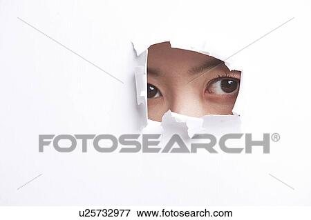 Stock Photo - Portrait of young woman peeking through a ripped paper hole. Fotosearch