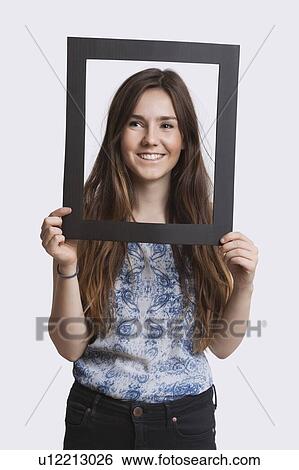 Stock Photograph - Portrait of young woman smiling through frame over white background. Fotosearch
