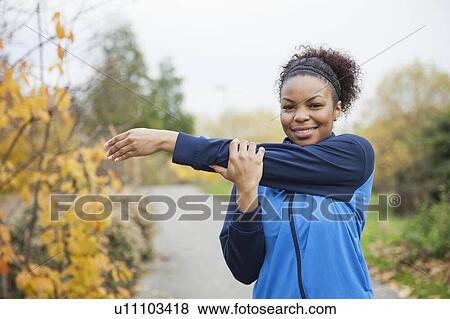 Stock Photo - Portrait of young woman stretching in park. Fotosearch