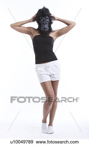 Stock Photo - Portrait of young woman wearing gorilla mask against white background. Fotosearch