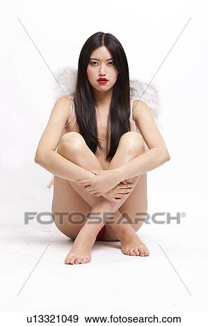 Stock Photo - Portrait of young woman with angel wings sitting on floor against white background. Fotosearch