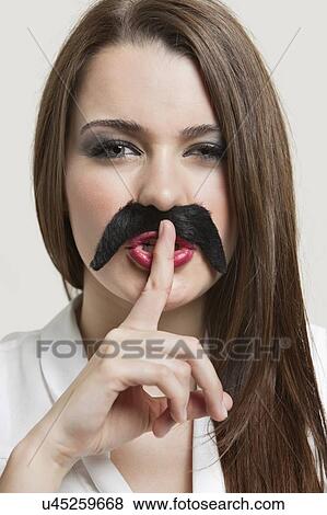 Portrait of young woman with fake mustache gesturing to be quiet over gray background View Large Photo Image Stock Photo - Portrait of young woman with fake mustache gesturing to be quiet over gray background. Fotosearch