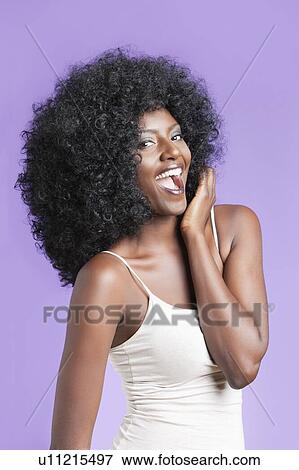 Stock Photo - Portrait of young woman with fizzy hairstyle standing over violet background. Fotosearch