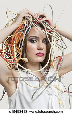 Stock Photo - Portrait of young woman with head tangled in colorful cables over gray background. Fotosearch