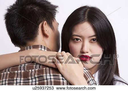 Stock Image - Portrait of young woman with red lips embracing man over white background. Fotosearch