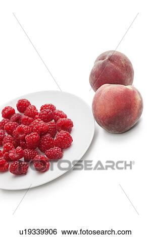 Stock Photograph - Raspberries in plate with peaches over white background. Fotosearch