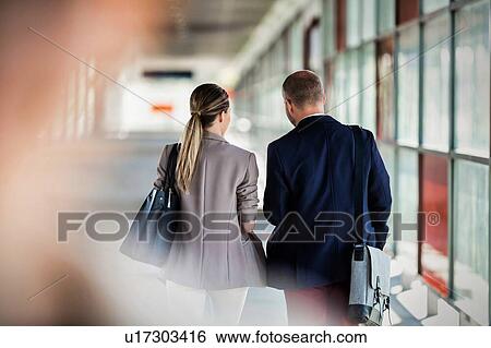 Stock Photograph - Rear view of businessman and businesswoman walking and talking. Fotosearch