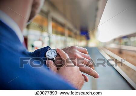 Stock Photo - Rear view of businessman looking at his watch while waiting in train station. Fotosearch