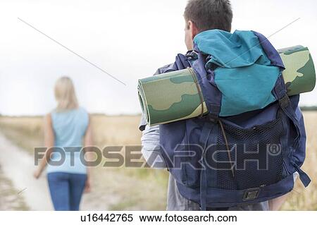 Rear view of male hiker carrying backpack with woman walking in foreground on field View Large Photo Image Stock Photography - Rear view of male hiker carrying backpack with woman walking in foreground on field. Fotosearch