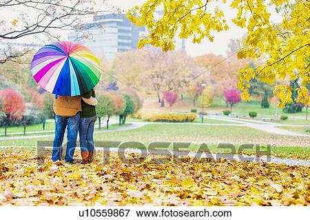 Rear view of man holding umbrella while enjoying the lovely view with his wife in park View Large Photo Image Stock Photo - Rear view of man holding umbrella while enjoying the lovely view with his wife in park. Fotosearch