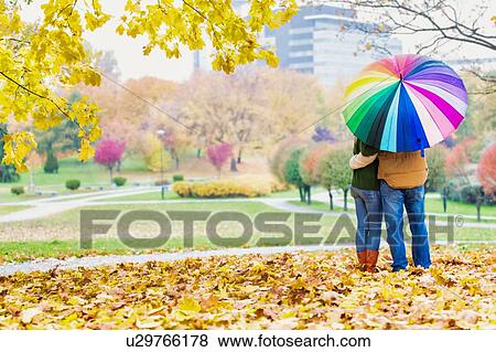 Rear view of man holding umbrella while enjoying the lovely view with his wife in park View Large Photo Image Stock Photo - Rear view of man holding umbrella while enjoying the lovely view with his wife in park. Fotosearch