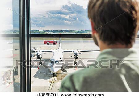 Stock Image - Rear view of man looking at the airplane through the window in airport. Fotosearch