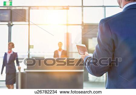 Rear view of mature businessman holding his passport and boarding pass at airport View Large Photo Image Picture - Rear view of mature businessman holding his passport and boarding pass at airport. Fotosearch