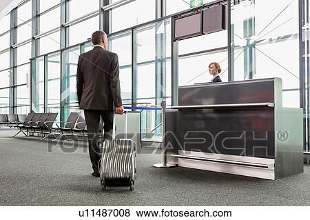 Stock Photo - Rear view of mature businessman walking with his suitcase on his gate for boarding in airport. Fotosearch