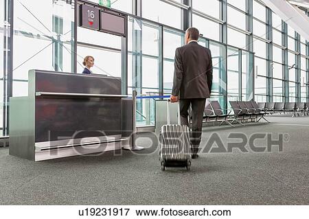 Rear view of mature businessman walking with his suitcase on his gate for boarding in airport View Large Photo Image Stock Photo - Rear view of mature businessman walking with his suitcase on his gate for boarding in airport. Fotosearch