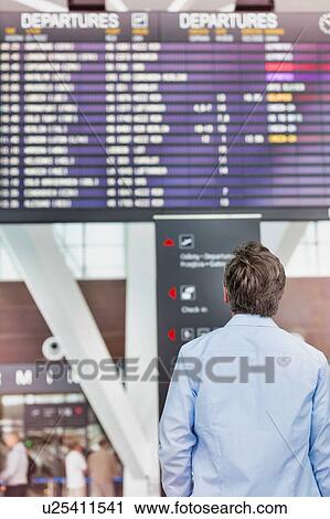 Stock Image - Rear view of mature man looking at his flght on screen in airport. Fotosearch
