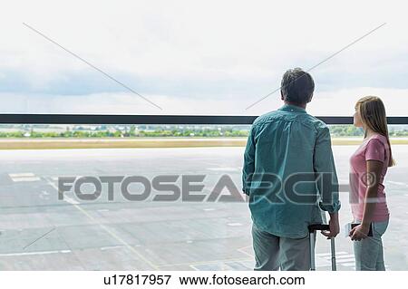 Stock Photo - Rear view of mature man looking through the window with his daughter in airport. Fotosearch
