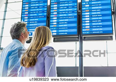 Stock Image - Rear view of mature man with his daughter looking at their flight on monitor in airport. Fotosearch