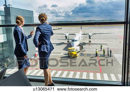 Stock Image - Rear view of young attractive airport staffs looking at the plane through the window in airport. Fotosearch