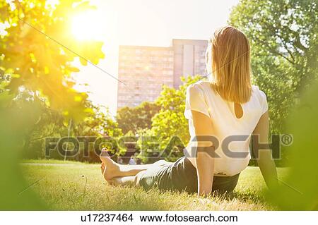 Picture - Rear view of young attractive businesswoman sitting on the grass while watching the sunset. Fotosearch