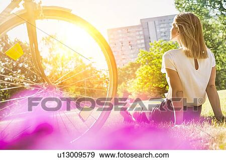 Stock Photo - Rear view of young attractive businesswoman sitting on the grass while watching the sunset. Fotosearch