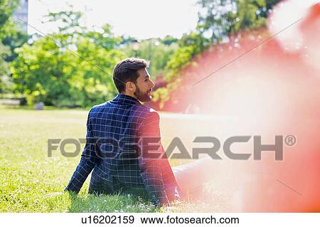Stock Photo - Rear view of young attractive businessman sitting on the grass during break. Fotosearch