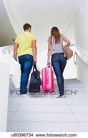 Picture - Rear view of young couple walking upstairs to check in on their room in hotel. Fotosearch