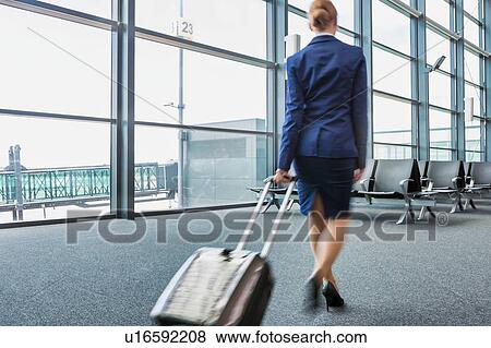 Stock Photo - Rear view of young flight attendant walking in airport with lens flare. Fotosearch