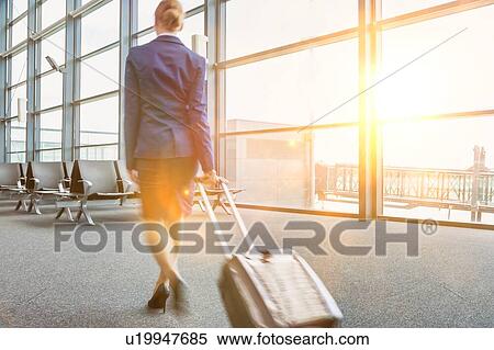 Stock Photography - Rear view of young flight attendant walking in airport with lens flare. Fotosearch