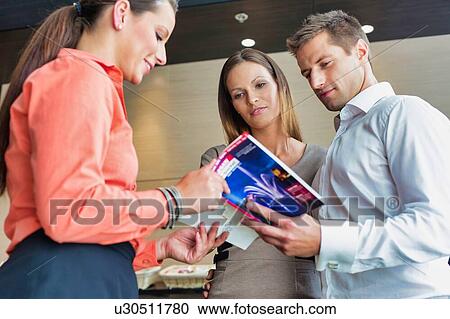 Receptionist showing brochure to business couple in hotel View Large Photo Image Stock Image - Receptionist showing brochure to business couple in hotel. Fotosearch