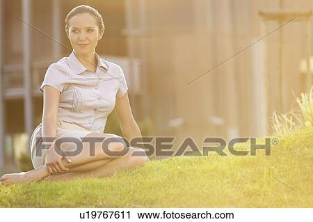 Stock Image - Relaxed young businesswoman sitting on lawn. Fotosearch