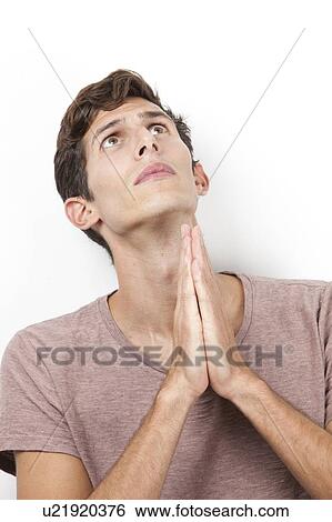 Stock Photograph - Sad young man with hands clasped praying over white background. Fotosearch
