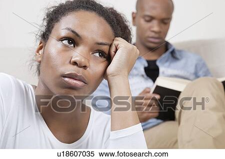 Stock Photography - Sad young woman with man reading book in background. Fotosearch