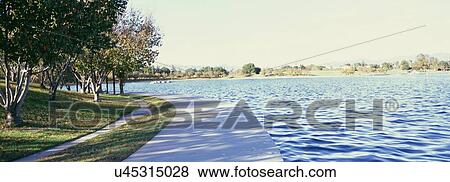 Scenic view of walkway beside calm lake View Large Photo Image Stock Photo - Scenic view of walkway beside calm lake. Fotosearch
