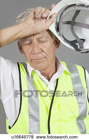 Senior construction worker wiping his brow over gray background View Large Photo Image Stock Photo - Senior construction worker wiping his brow over gray background. Fotosearch