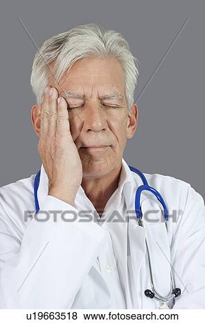 Stock Photo - Senior doctor suffering from headache over gray background. Fotosearch