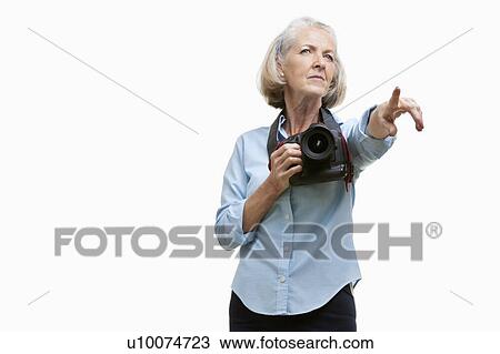 Stock Image - Senior female photographer with camera gesturing against white background. Fotosearch