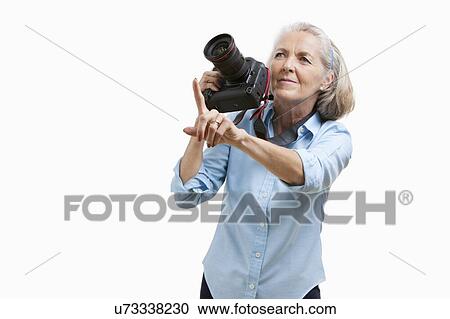 Senior female photographer with camera gesturing against white background View Large Photo Image Stock Image - Senior female photographer with camera gesturing against white background. Fotosearch