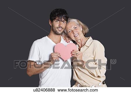 Stock Photo - Senior woman and young man holding red paper heart against black background. Fotosearch