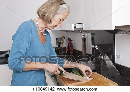 Stock Image - Senior woman chopping vegetables at kitchen counter. Fotosearch