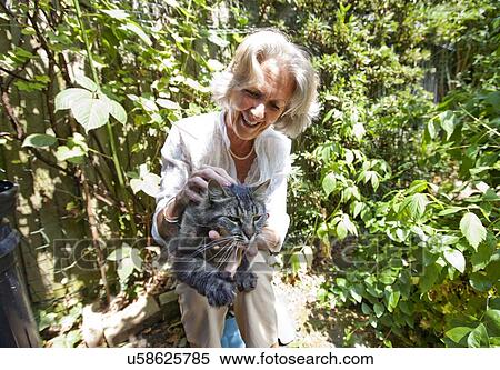 Stock Photography - Senior woman cuddling cat while sitting in garden. Fotosearch