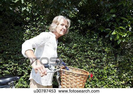 Stock Image - Senior woman looking away while standing with bicycle at backyard. Fotosearch