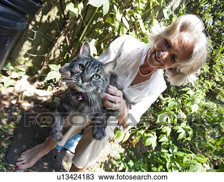 Stock Image - Senior woman stroking cat while sitting in garden. Fotosearch