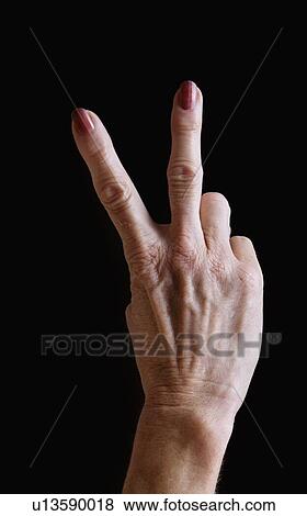 Stock Photo - Senior woman's hands gesturing peace sign against black background. Fotosearch