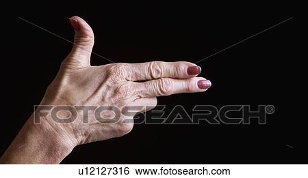 Stock Photograph - Senior woman's hands making shooting gesture against black background. Fotosearch