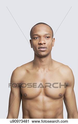 Stock Image - Shirtless young man standing against gray background. Fotosearch