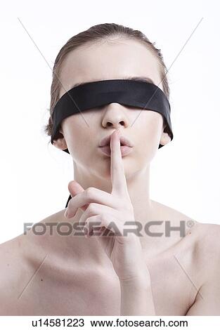 Stock Image - Shirtless young woman with blindfold gesturing to be silent against white background. Fotosearch
