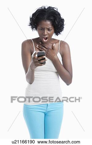 Shocked young woman looking at cell phone over white background View Large Photo Image Stock Image - Shocked young woman looking at cell phone over white background. Fotosearch