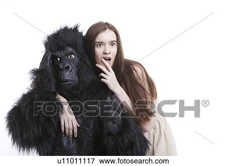 Stock Photo - Shocked young woman with irritated man in gorilla costume against white background. Fotosearch